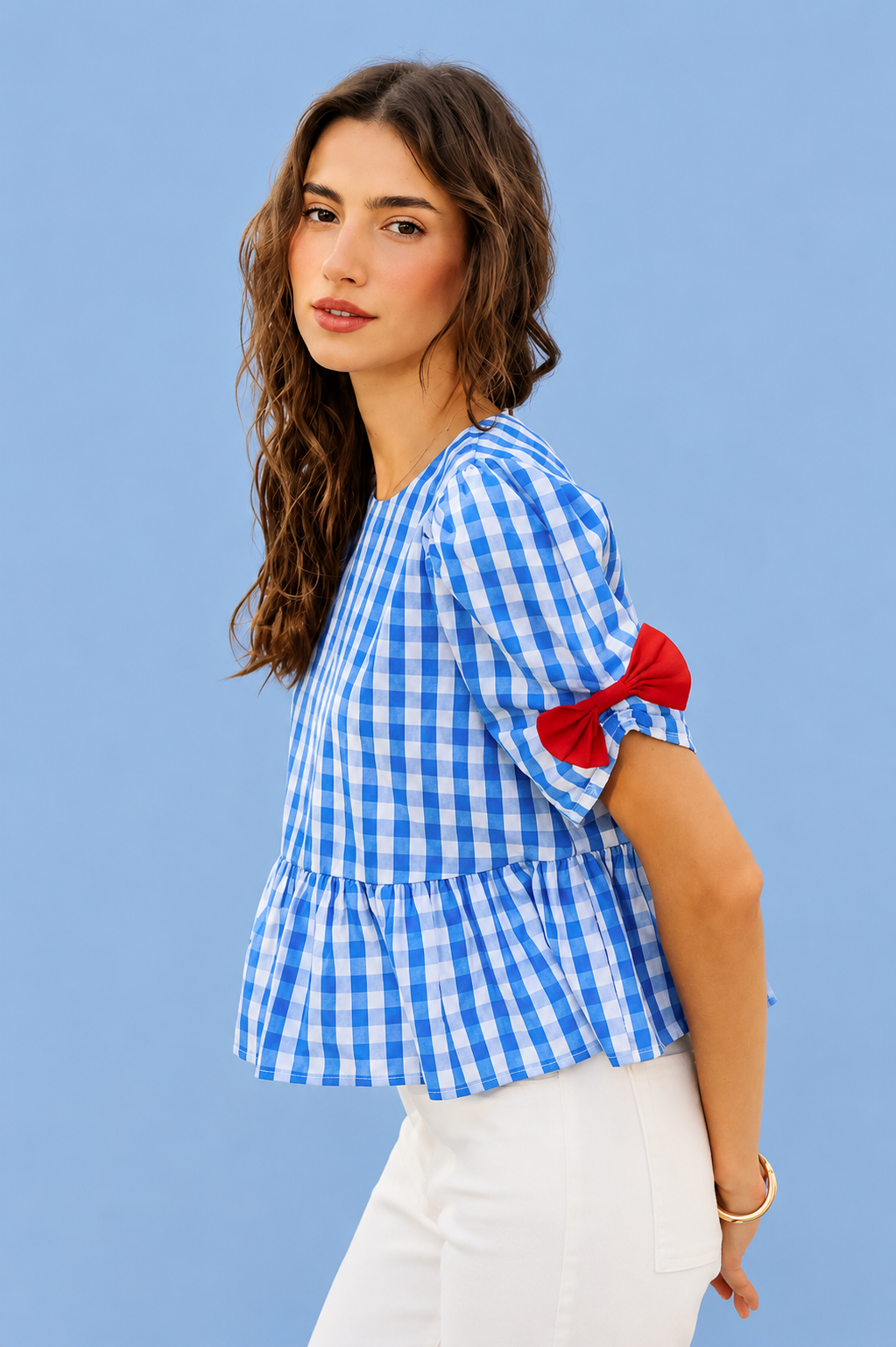 Woman wearing SO ME blue gingham ribbon detail short sleeve blouse featuring bow accents, peplum silhouette, and lightweight summer styling. Side View 2