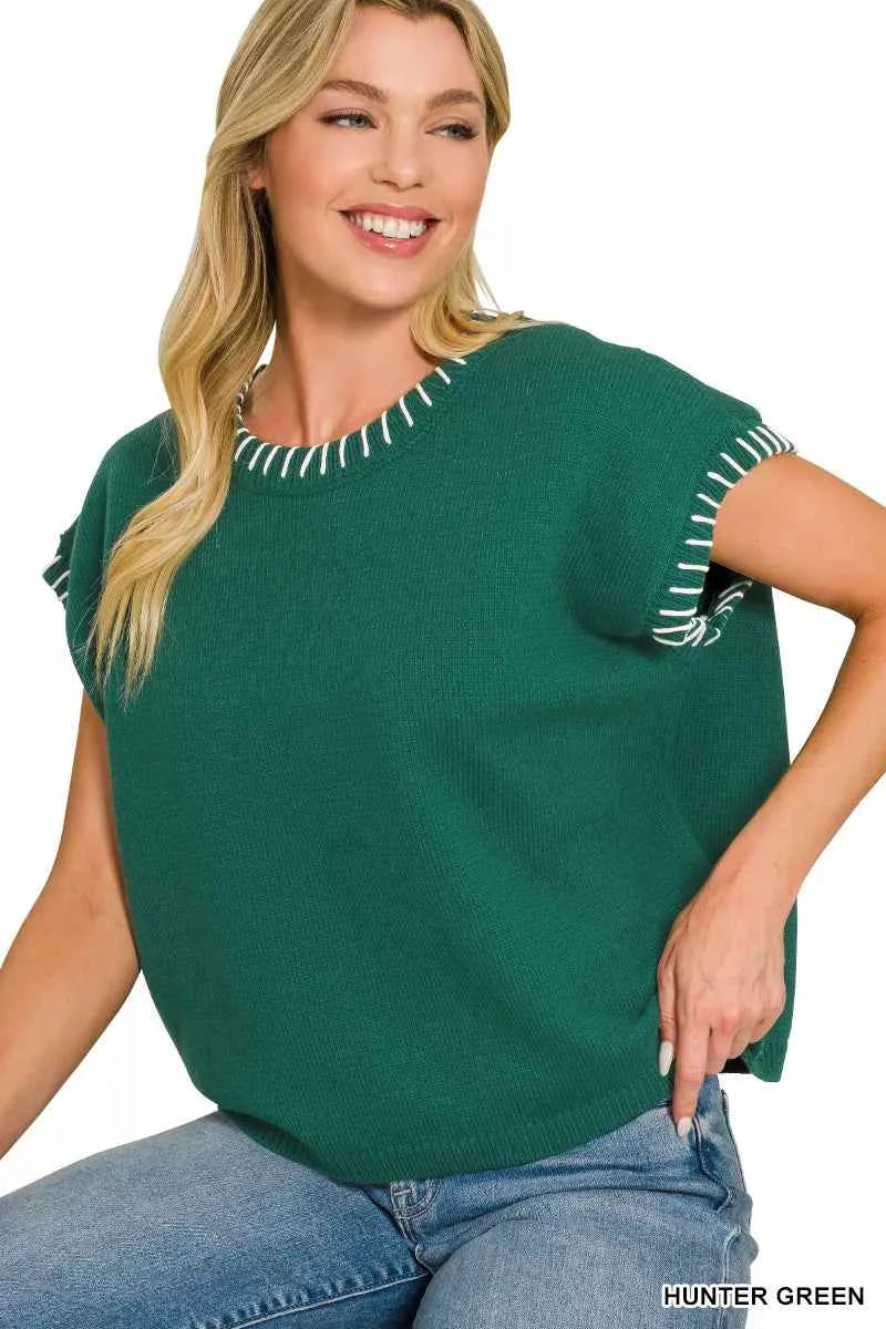 Woman wearing a Zenana hunter green oversized knit sweater vest with white contrast stitch detailing, cap sleeves, and a relaxed fit styled with denim jeans. Sitting