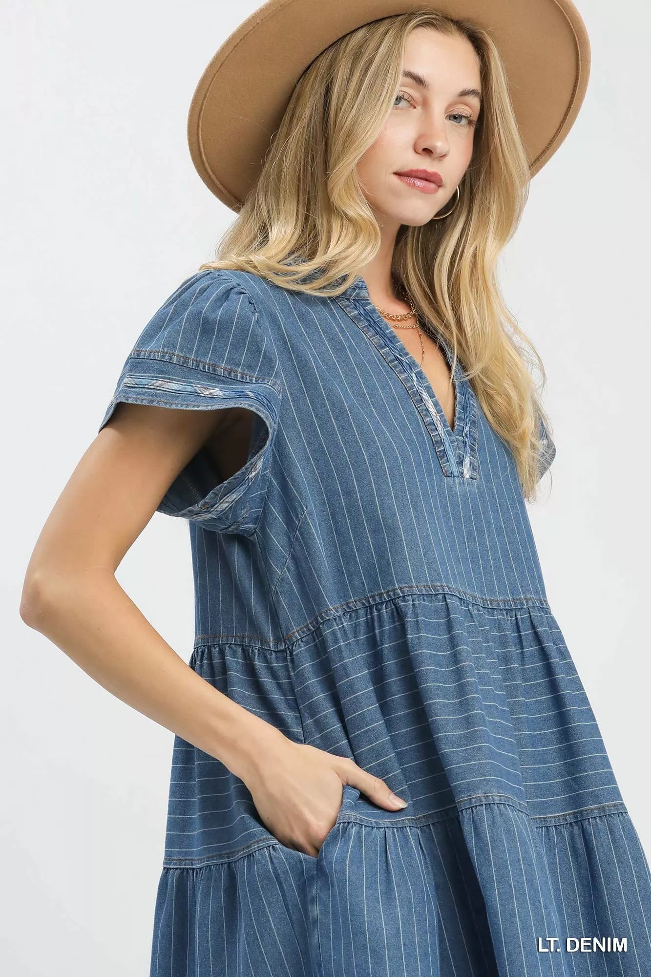 Woman wearing a light denim pinstripe chambray tiered babydoll dress with flutter sleeves and pockets by Umgee Side Pocket View
