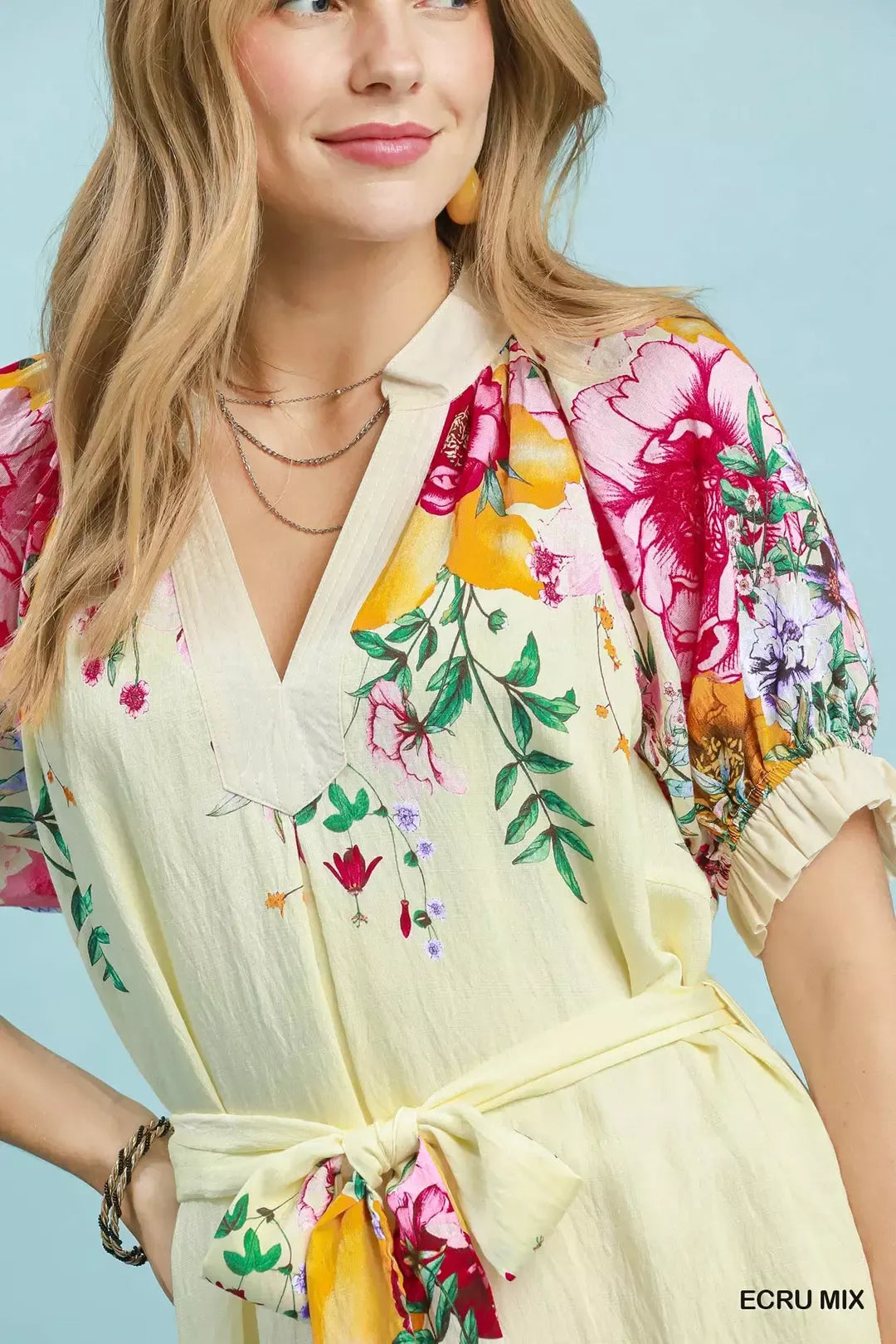 Woman wearing an Umgee ecru floral border print midi dress with a waist tie, puff sleeves, and colorful floral details. Close View