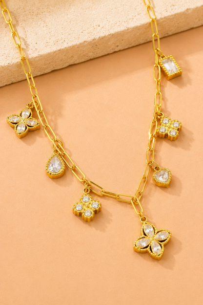 18K gold stainless steel charm link necklace featuring crystal clover, heart, floral, and geometric charms on a paperclip chain. Flat Lay