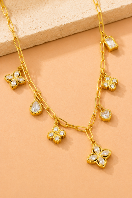 18K gold stainless steel charm link necklace featuring crystal clover, heart, floral, and geometric charms on a paperclip chain. Flat Lay