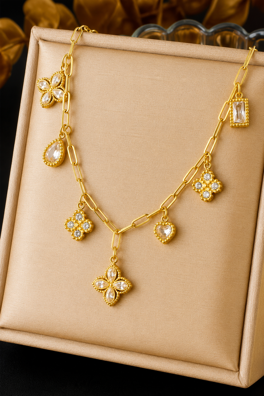 18K gold stainless steel charm link necklace featuring crystal clover, heart, floral, and geometric charms on a paperclip chain. View in box