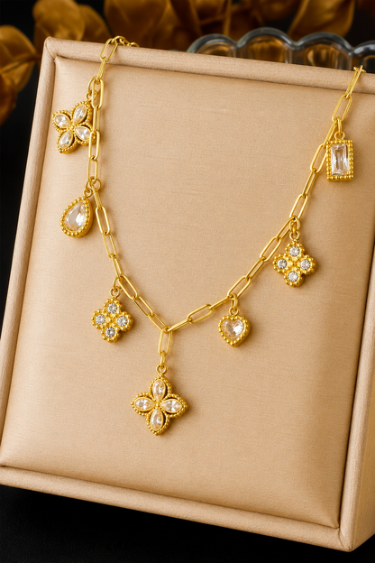18K gold stainless steel charm link necklace featuring crystal clover, heart, floral, and geometric charms on a paperclip chain. View in box