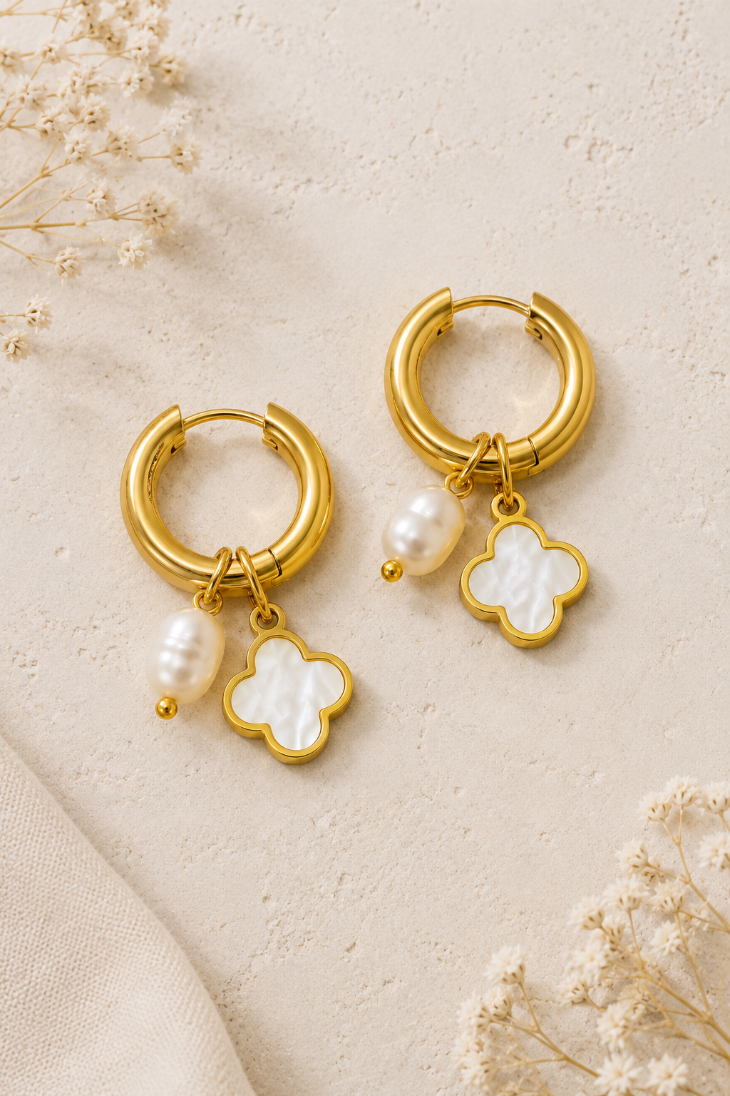 18K gold stainless steel huggie hoop earrings featuring a white clover charm and pearl drop displayed on a neutral boutique background.