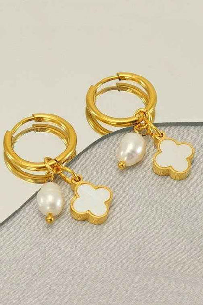 18K gold stainless steel huggie hoop earrings featuring a white clover charm and pearl drop displayed on a neutral boutique background.