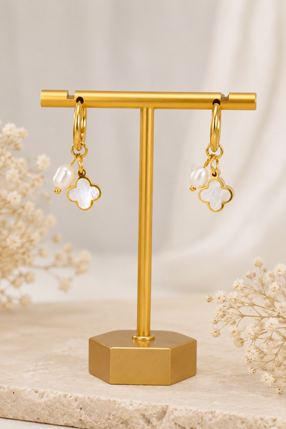 18K gold stainless steel huggie hoop earrings featuring a white clover charm and pearl drop displayed on a neutral boutique background.