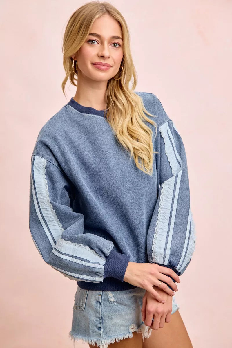 Woman wearing a washed denim lace contrast sweatshirt with long sleeves and relaxed fit by BiBi.
