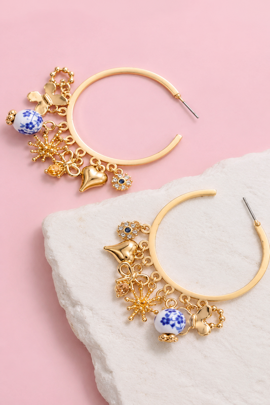 Two gold hoop earrings with blue and white porcelain beads and gold charms on a white stone over a pink background.