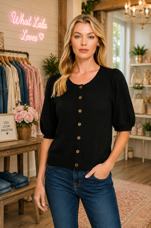 A woman modeling a black puff-sleeve button-front top with scalloped neckline, paired with blue jeans in a boutique setting. from Zenana