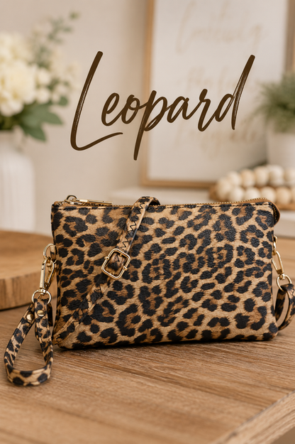 A leopard print wristlet clutch bag with a matching wrist strap and gold-tone hardware, displayed on a wooden surface with a blurred home decor background and the word 'Leopard' written in script above.