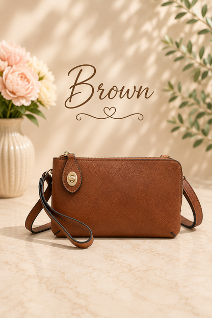A brown faux-leather crossbody handbag with a wristlet strap and a gold-tone snap button, displayed on a beige marble surface with a floral vase and leafy branches in the background, with the word 'Brown' written above.