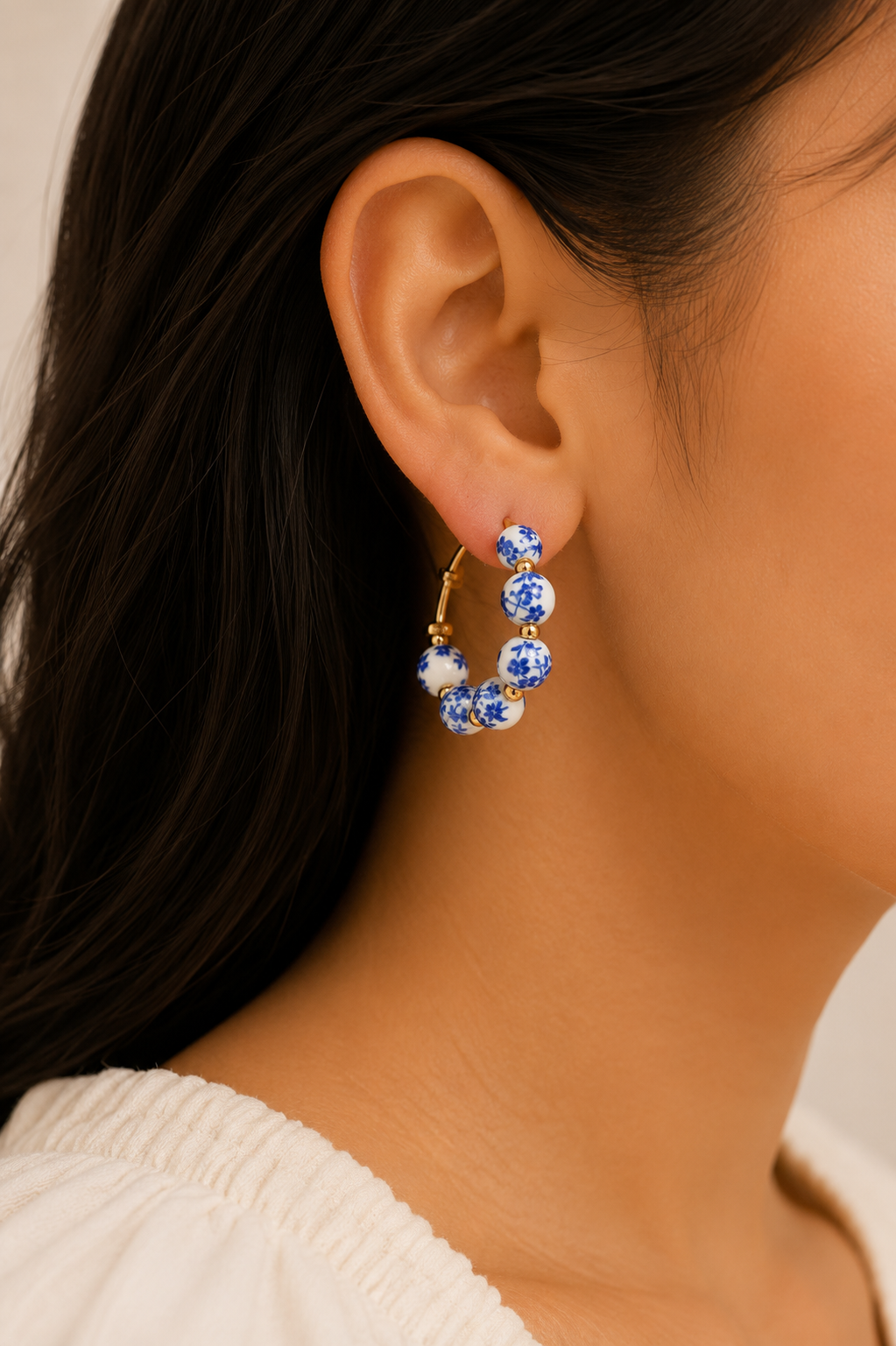 A close-up of a model's ear wearing a gold hoop earring adorned with blue and white floral beads.