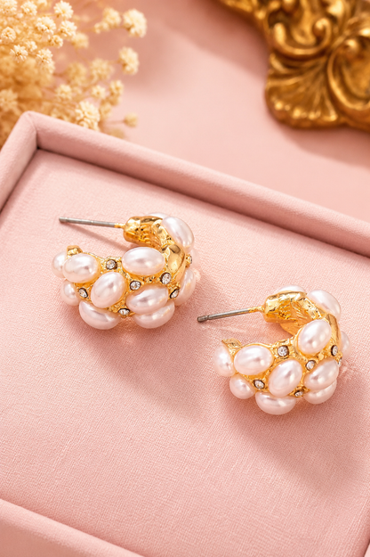 Gold hoop earrings adorned with faux pearl clusters and small crystal accents, displayed on a pink jewelry box.