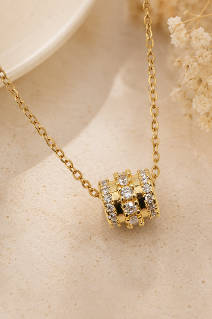 Gold metal chain necklace with a barrel-shaped slider pendant featuring three rows of clear round crystals.