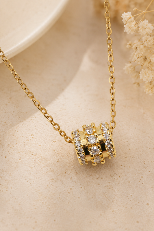 Gold metal chain necklace with a barrel-shaped slider pendant featuring three rows of clear round crystals.