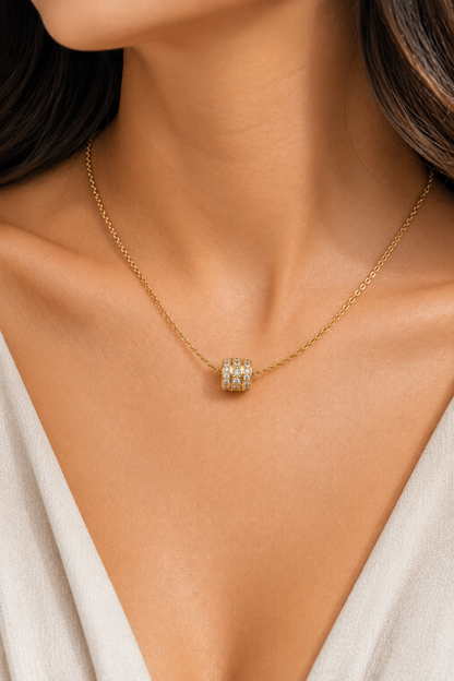 Gold chain necklace on a person featuring a small barrel-shaped slider pendant set with three rows of clear stones.