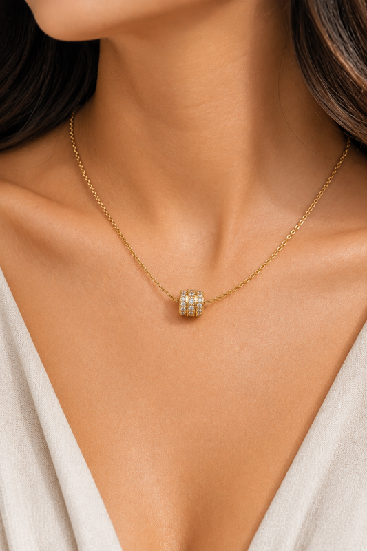 Gold chain necklace on a person featuring a small barrel-shaped slider pendant set with three rows of clear stones.