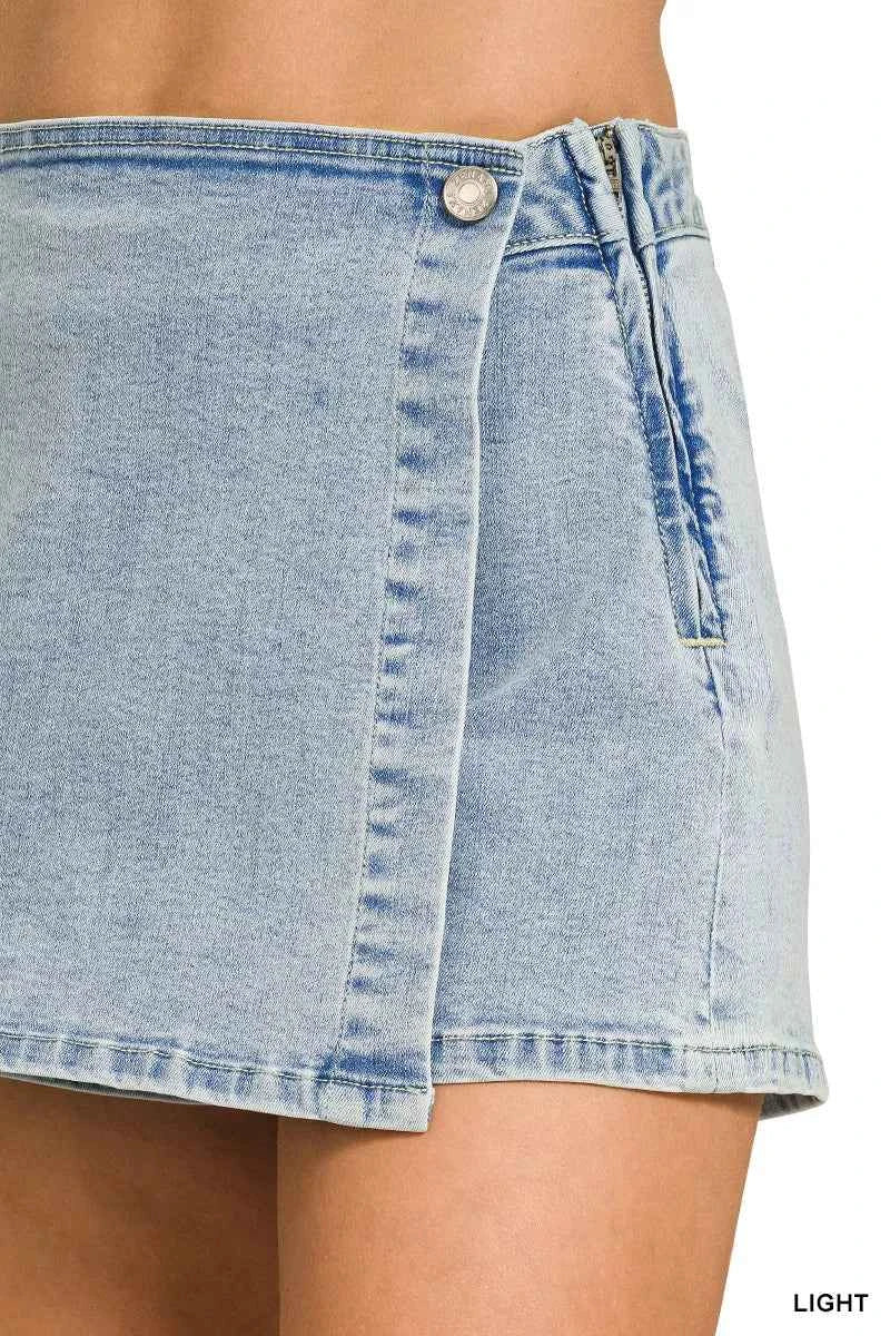 Close view of a Zenana light wash denim wrap skort featuring a button closure, asymmetrical overlap design, mini length, and built-in shorts.
