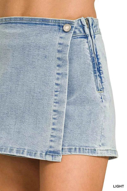 Close view of a Zenana light wash denim wrap skort featuring a button closure, asymmetrical overlap design, mini length, and built-in shorts.