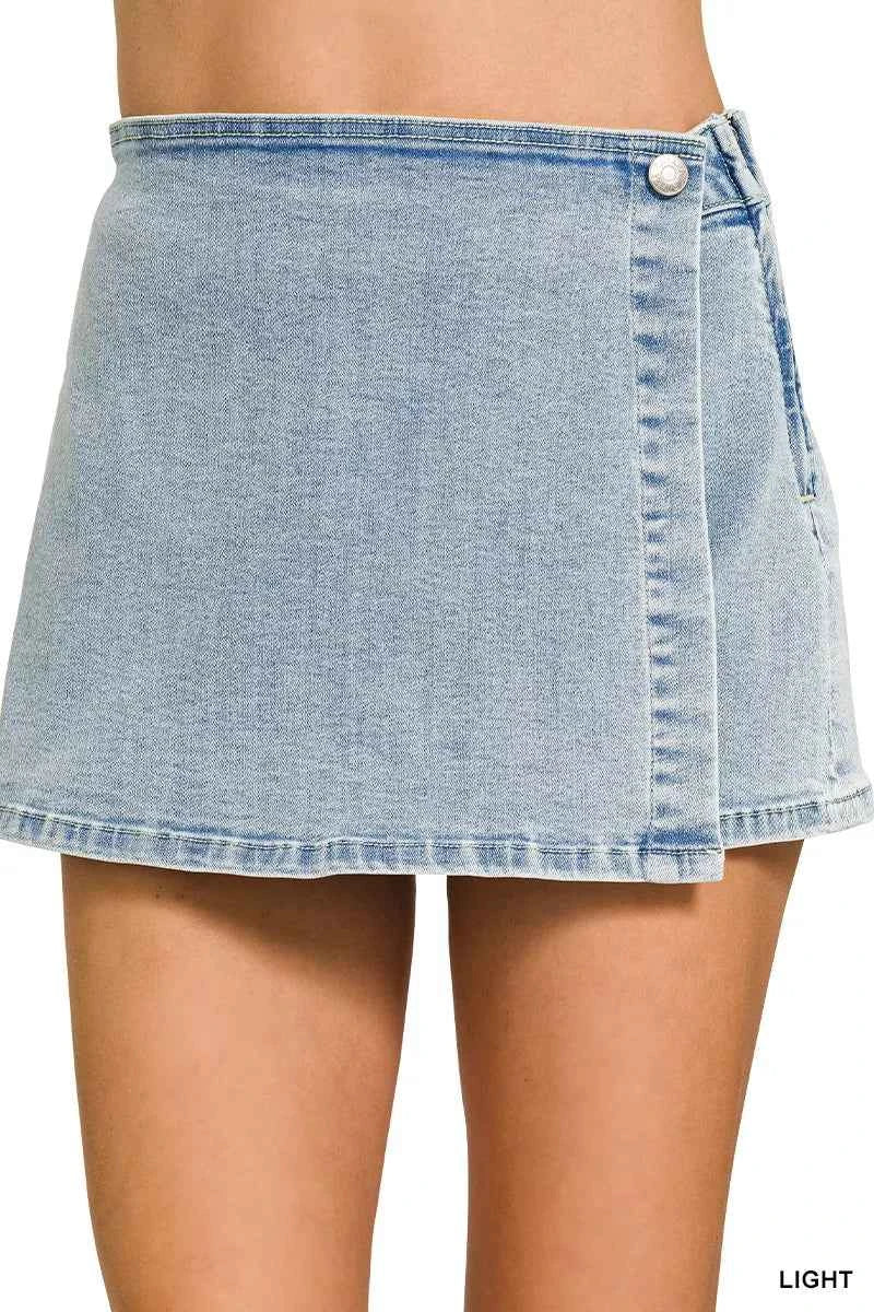 Front view of a Zenana light wash denim wrap skort featuring a button closure, asymmetrical overlap design, mini length, and built-in shorts.