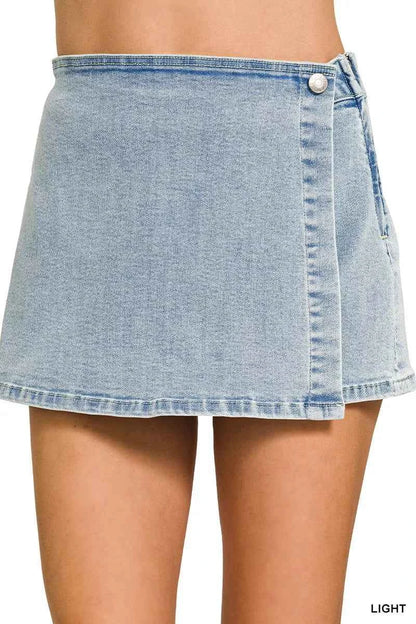 Front view of a Zenana light wash denim wrap skort featuring a button closure, asymmetrical overlap design, mini length, and built-in shorts.