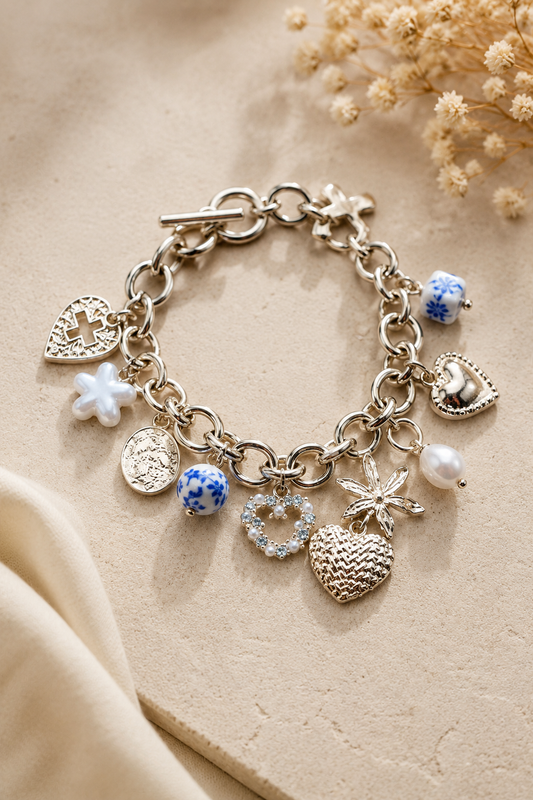 Gold charm toggle bracelet with blue porcelain hearts, cross, pearl, bow, floral, and crystal charms. Flat Lay 2