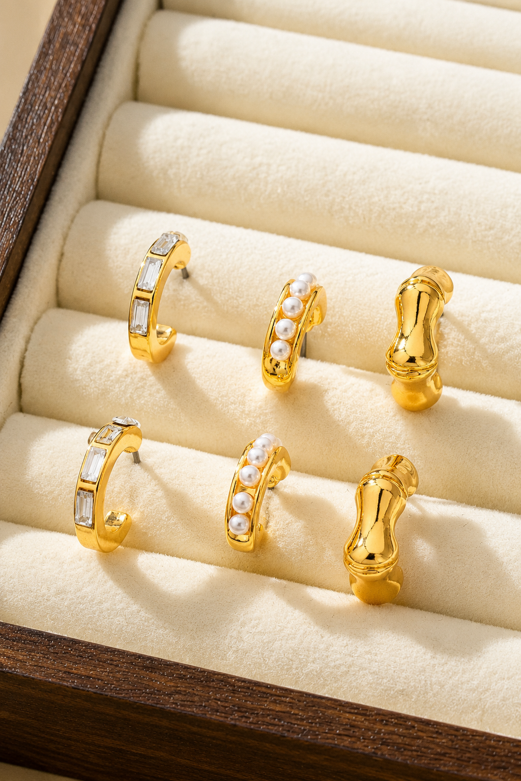 Gold hoop earring trio set featuring pearl huggies, sculptural C-hoops, and baguette crystal hoops. Shown in box