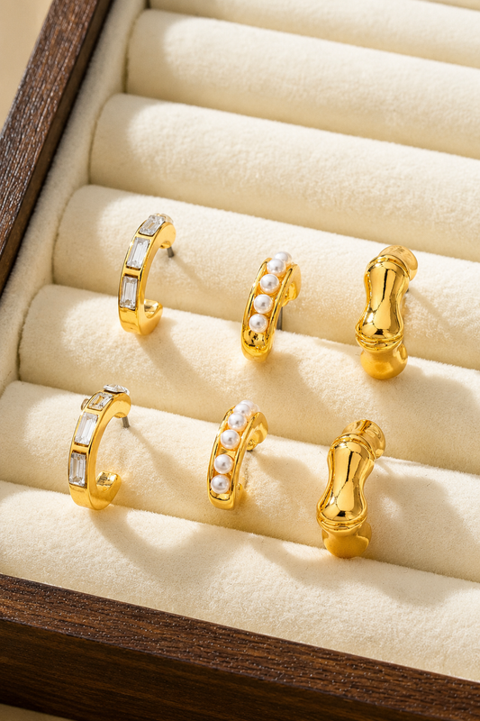 Gold hoop earring trio set featuring pearl huggies, sculptural C-hoops, and baguette crystal hoops. Shown in box