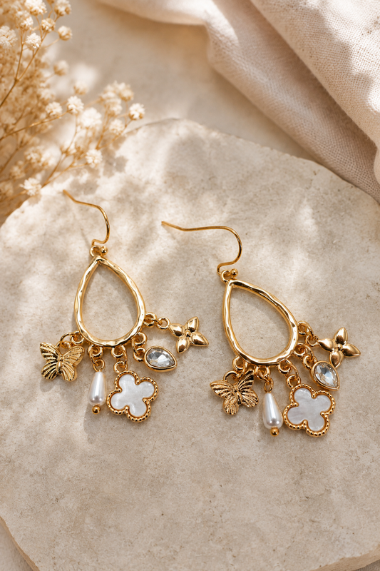 Gold multi-charm teardrop earrings with butterfly, shell clover, pearl, crystal, and floral charms. Flat Lay