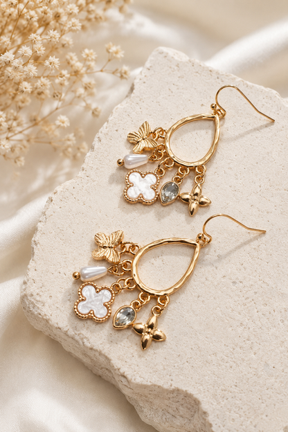 Gold multi-charm teardrop earrings with butterfly, shell clover, pearl, crystal, and floral charms. Flat Lay 2