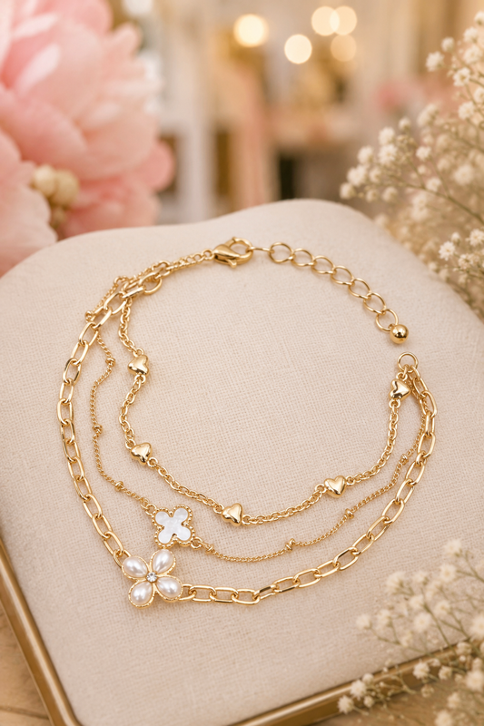 Gold multi-layer bracelet featuring a pearl flower charm, clover charm, heart accents, and layered chains.