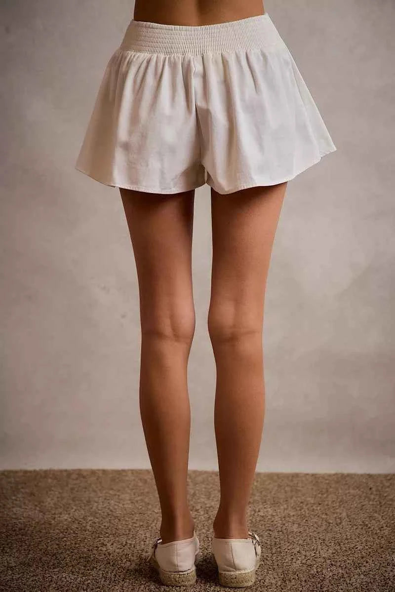 SO ME white denim bubble skort featuring a flared silhouette, smocked back waistband, built-in shorts, and comfortable cotton construction. Back View