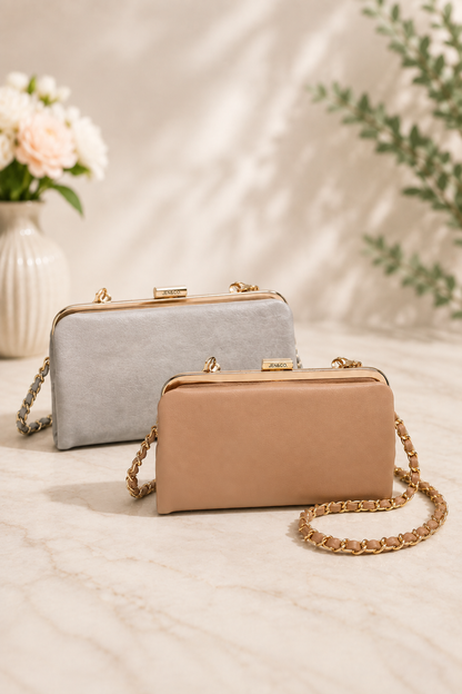 Two elegant clutch bags with gold-tone chain straps, displayed on a light marble surface. The front bag is a warm tan/beige color, and the bag behind it is a light gray color.