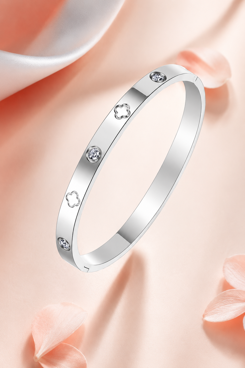 A polished silver bangle bracelet with small clear gemstone accents, displayed on a soft peach-pink background with decorative rose petals.