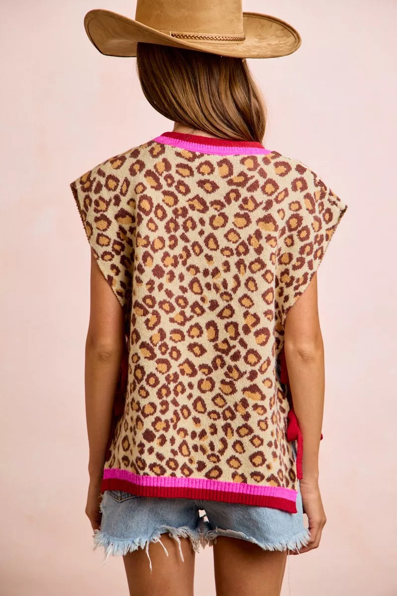 Woman wearing BiBi leopard print side tie sweater vest with pink contrast trim, adjustable side ties, and relaxed fit paired with denim shorts. Back View