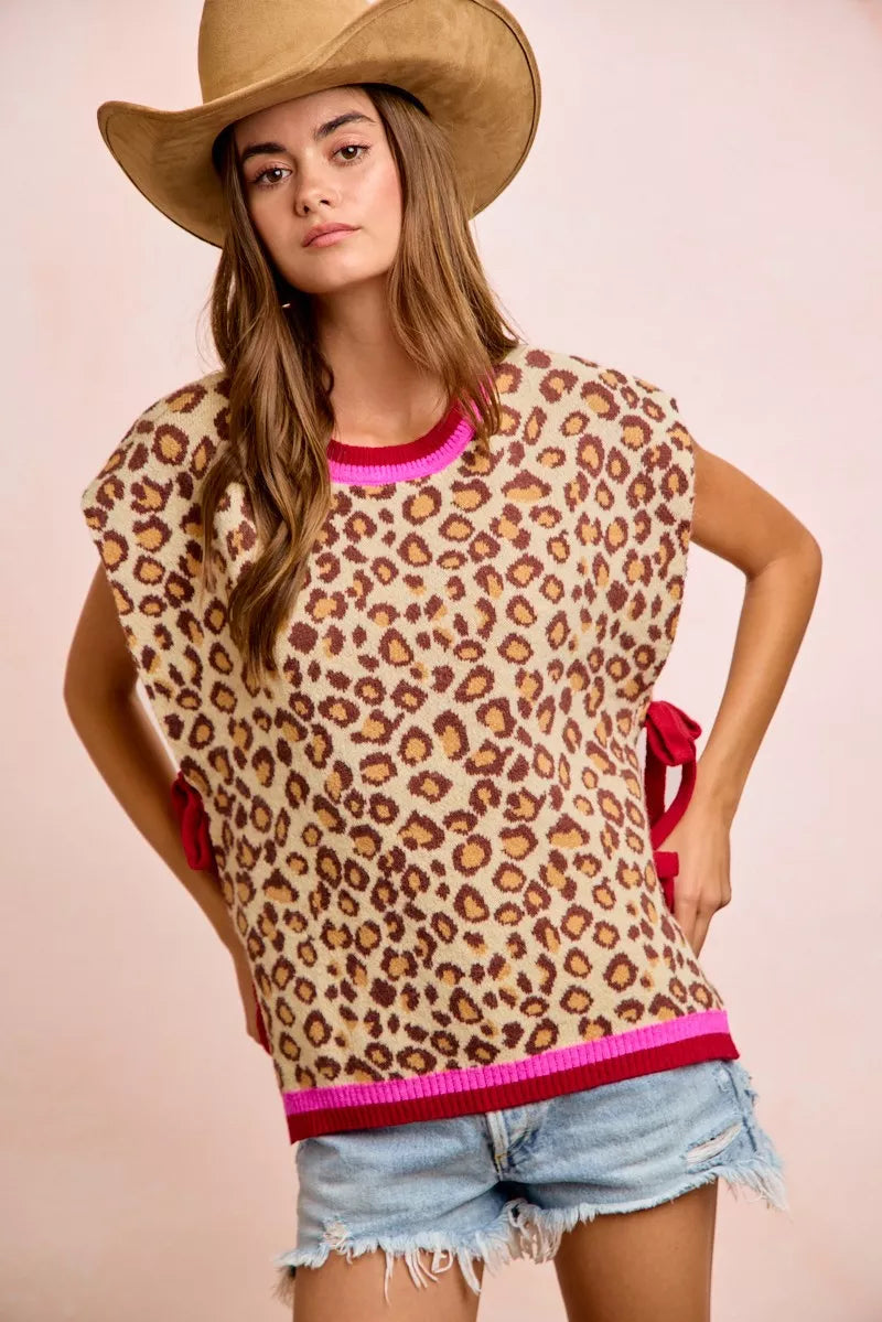 Woman wearing BiBi leopard print side tie sweater vest with pink contrast trim, adjustable side ties, and relaxed fit paired with denim shorts. Front View