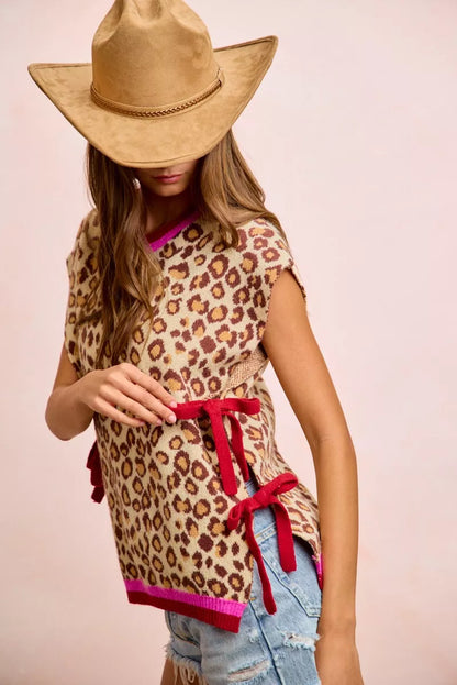 Woman wearing BiBi leopard print side tie sweater vest with pink contrast trim, adjustable side ties, and relaxed fit paired with denim shorts. Side View 4