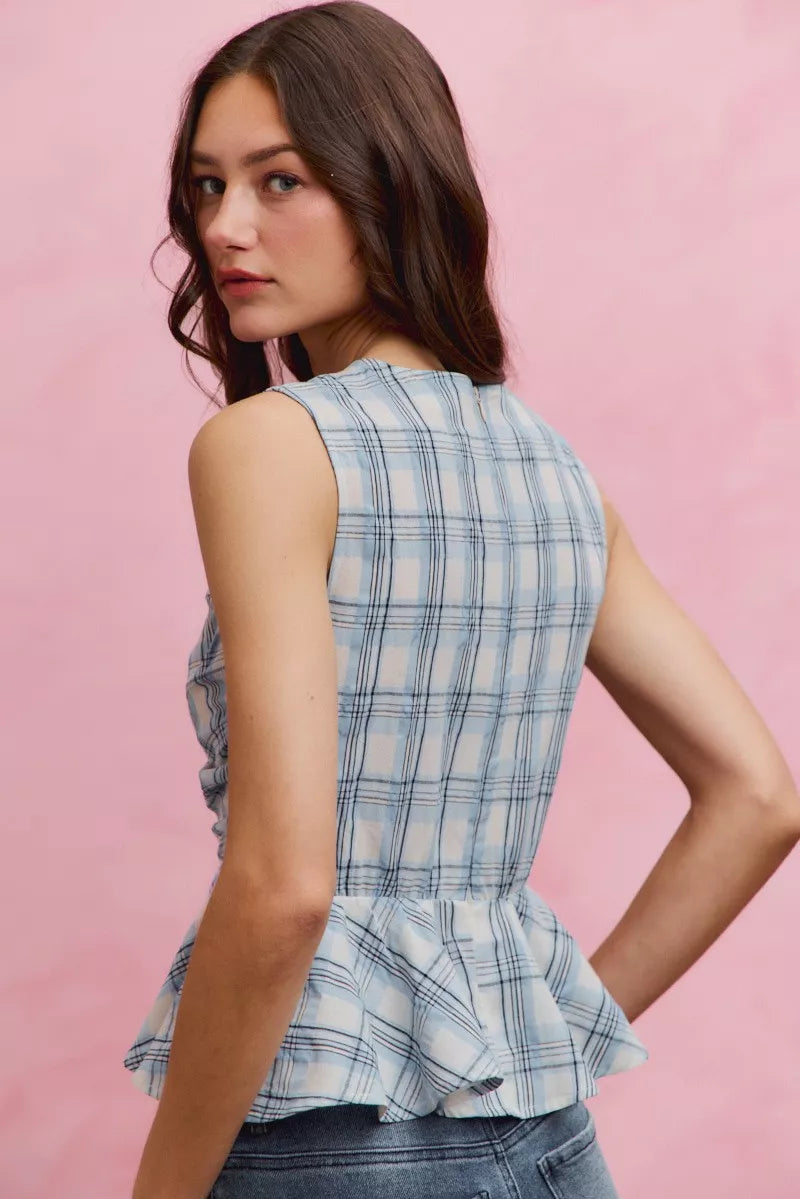 Woman wearing SO ME blue plaid sleeveless peplum top with ruffle front detail, shirred waist, and lightweight cotton fabric. Back View