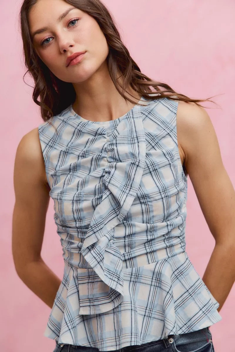 Woman wearing SO ME blue plaid sleeveless peplum top with ruffle front detail, shirred waist, and lightweight cotton fabric. Close View
