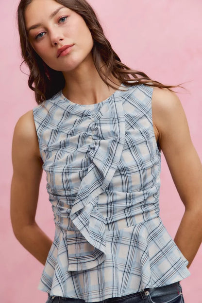 Woman wearing SO ME blue plaid sleeveless peplum top with ruffle front detail, shirred waist, and lightweight cotton fabric. Close View