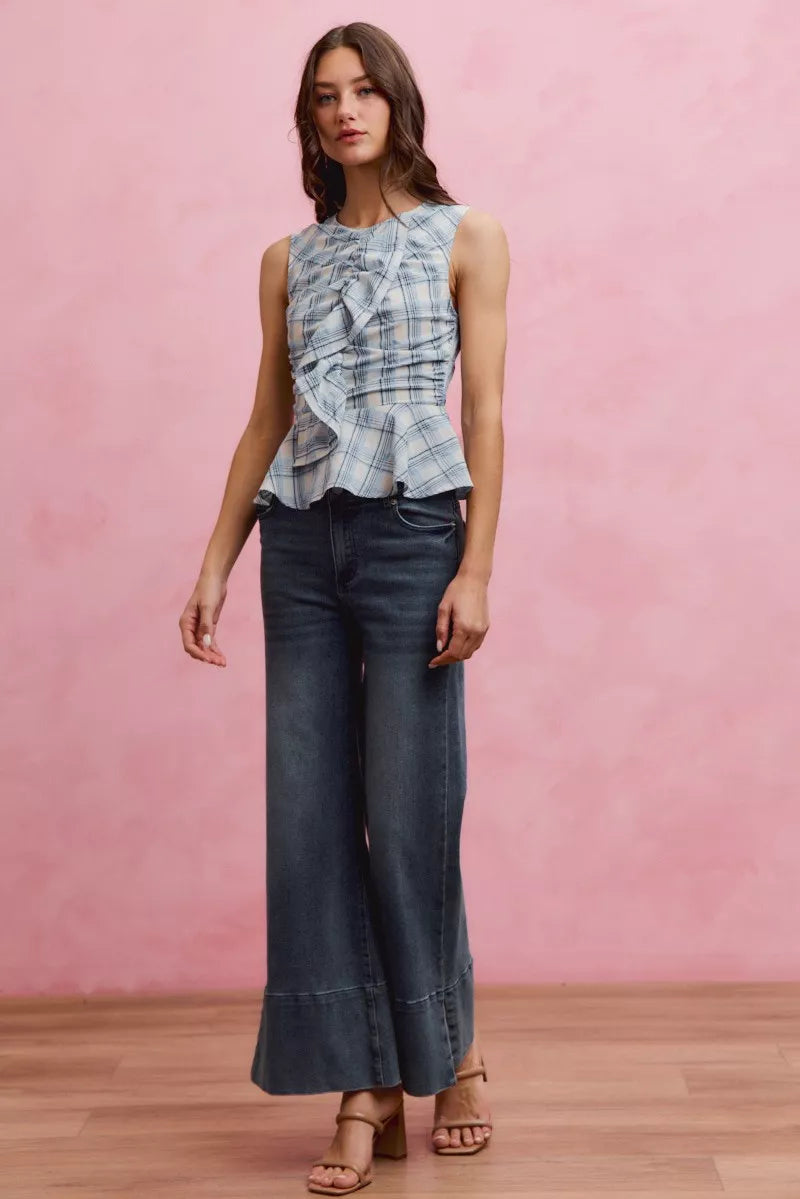 Woman wearing SO ME blue plaid sleeveless peplum top with ruffle front detail, shirred waist, and lightweight cotton fabric. Full View