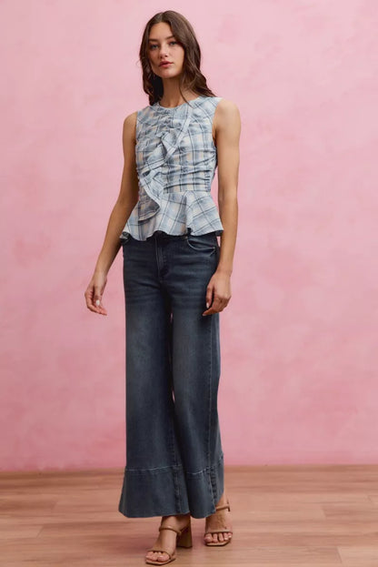 Woman wearing SO ME blue plaid sleeveless peplum top with ruffle front detail, shirred waist, and lightweight cotton fabric. Full View