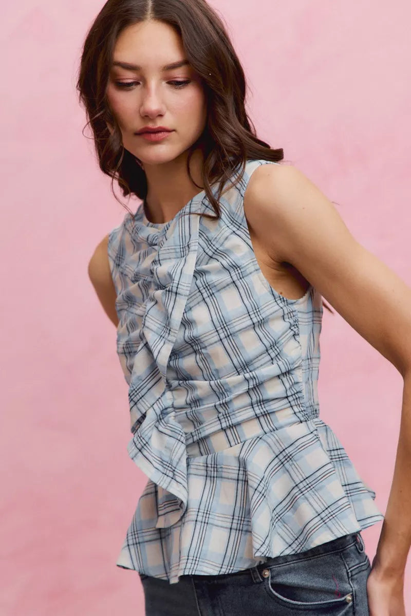 Woman wearing SO ME blue plaid sleeveless peplum top with ruffle front detail, shirred waist, and lightweight cotton fabric. Side View 2