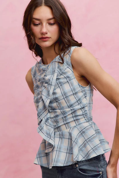 Woman wearing SO ME blue plaid sleeveless peplum top with ruffle front detail, shirred waist, and lightweight cotton fabric. Side View 2