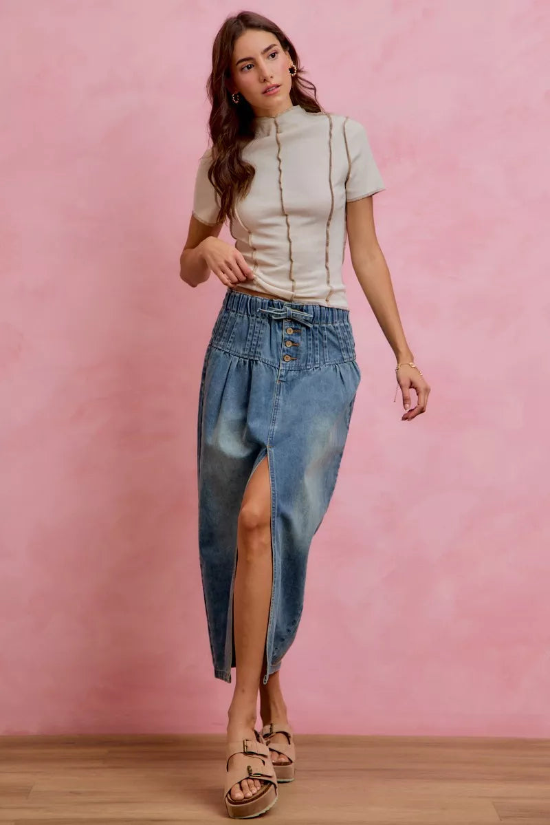 Woman wearing SO ME high waist button front denim maxi skirt with drawstring waistband, pleated waist detail, distressed wash, and front slit.