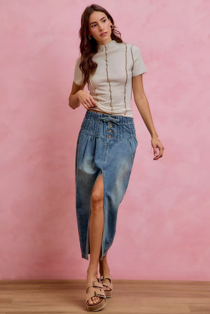 Woman wearing SO ME high waist button front denim maxi skirt with drawstring waistband, pleated waist detail, distressed wash, and front slit.