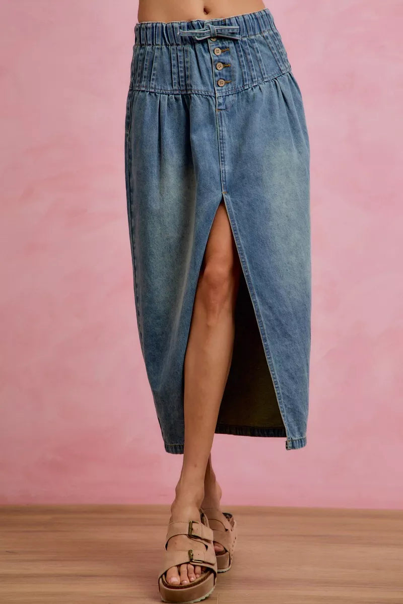 Woman wearing SO ME high waist button front denim maxi skirt with drawstring waistband, pleated waist detail, distressed wash, and front slit. Front View