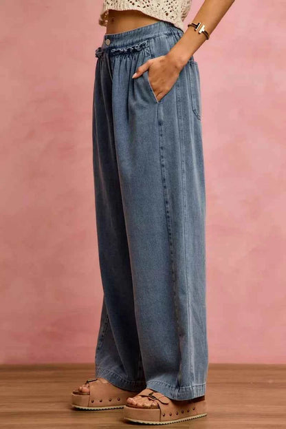 Woman wearing SO ME mid rise wide leg jeans with ruffled front detailing, elastic waistband, and lightweight denim construction.
 Side View