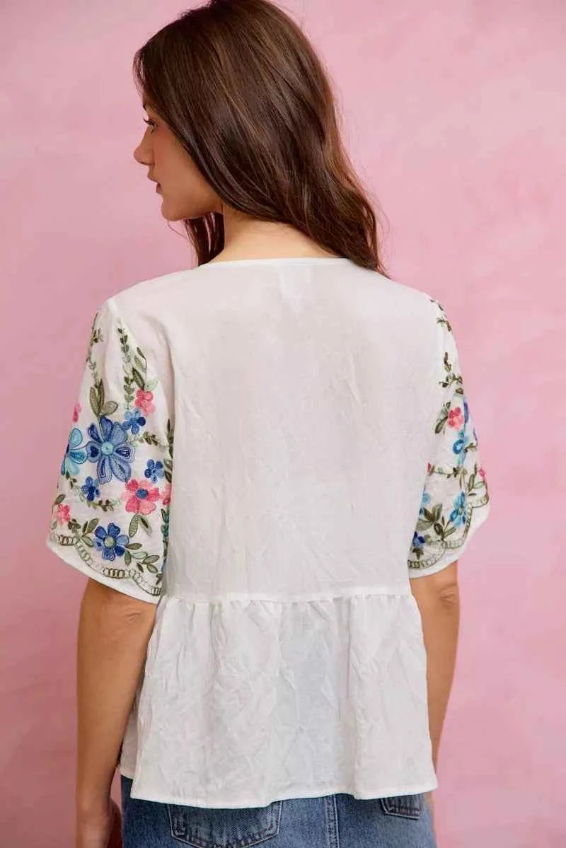 Woman wearing SO ME off white floral embroidered babydoll blouse top featuring colorful floral embroidery, flowy silhouette, short sleeves, and feminine everyday style. Back View